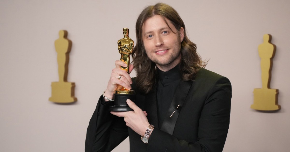 Ludwig Göransson holds an Academy Award close to his face on the Oscars red carpet.