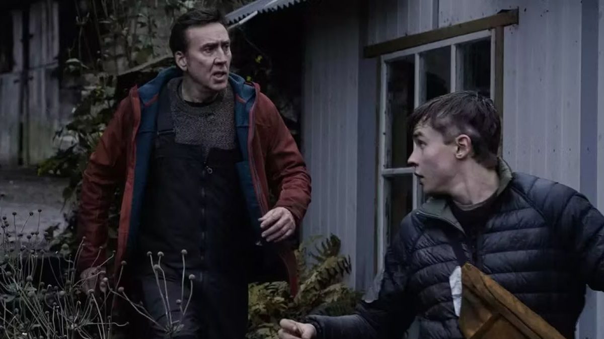 Nicolas Cage and Maxwell Jenkins walk past a farmhouse in a dark, blue toned lit image
