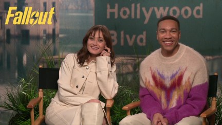 Image of Ella Purnell and Aaron Moten sitting in director chairs during a virtual press junket. Purnell is a white woman with shoulder-length brown hair and wearing an off-white jacket over an off-white dress and knee-high boots. Moten is a Black man with short black hair wearing a sweater that's white at the shoulders with a purple gradient pattern down the middle of it.