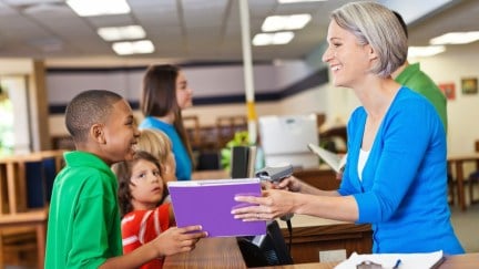 A school librarians hands a book to a child