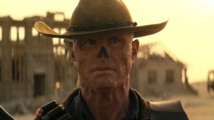 Walton Goggins as The Ghoul in Prime Video's 'Fallout.' He is a man who has been irradiated to the point of his skin being red and wrinkly, having no hair, and no nose. He's wearing a cowboy hat and strapped with weapons as he walks through the Wasteland.