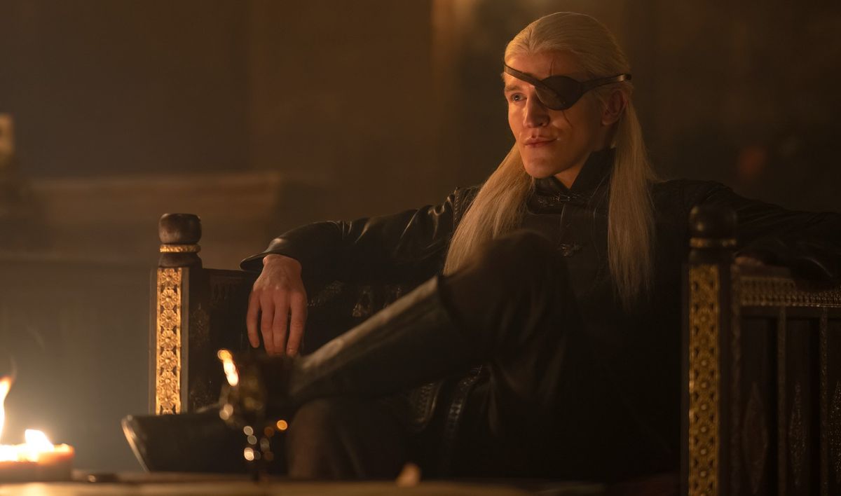 Aemond Targaryen sits in a chair in a fire lit room in "House of the Dragon"