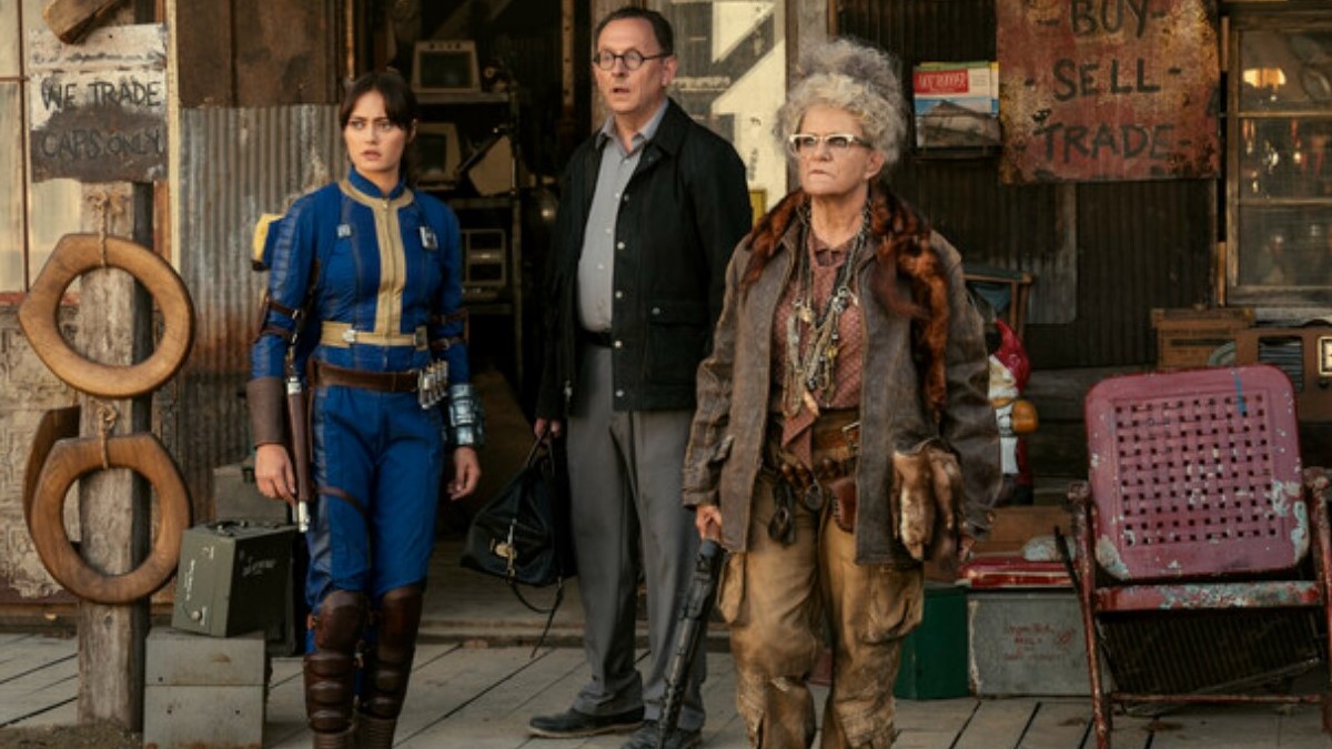 Ella Purnell as Lucy, Michael Emerson as Wilzig, and Dale Dickey as Ma June in a scene from Prime Video's 'Fallout.' They are standing together outside Ma June's Sundries and all looking at the same thing off-camera.