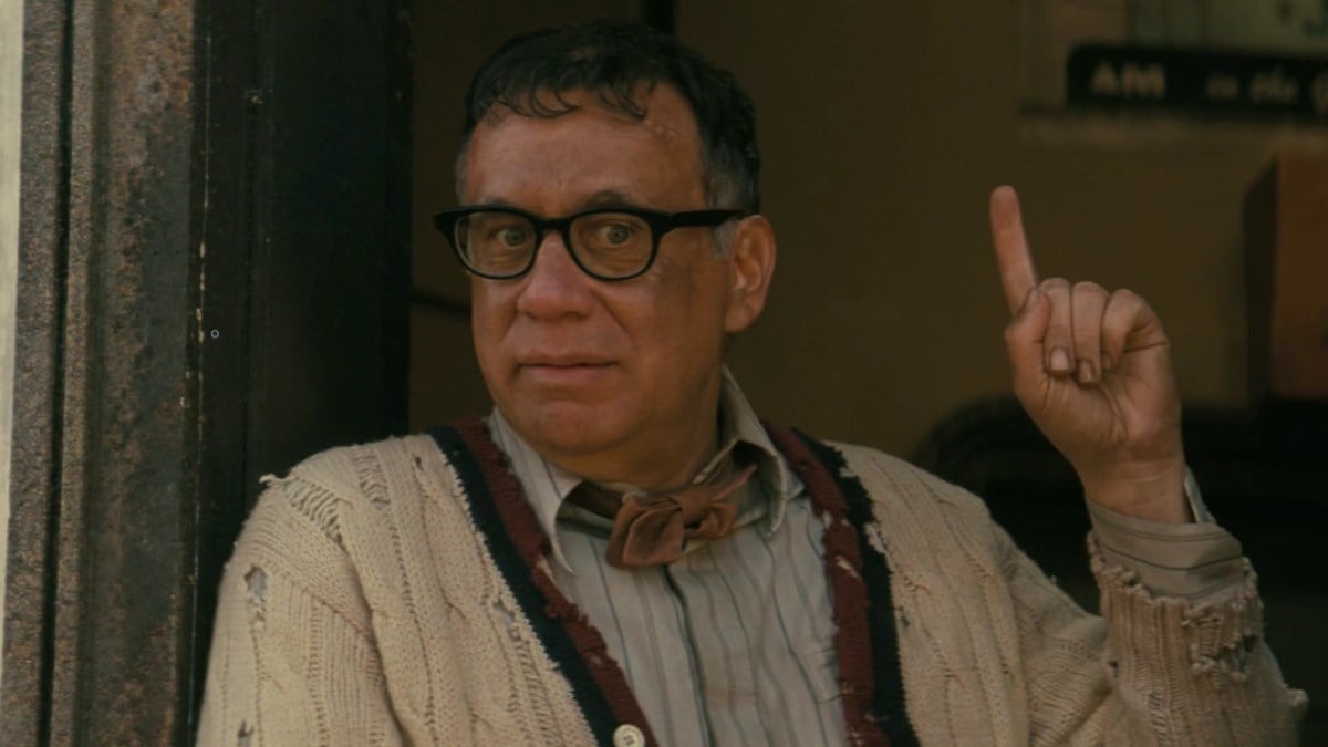 Fred Armisen as Carl in a scene from Prime Video's 'Fallout.' He is wearing black-rimmed glasses, a reddish bow tie, and a knit sweater over a buttondown. He's pointing a finger up calling someone's attention to something.