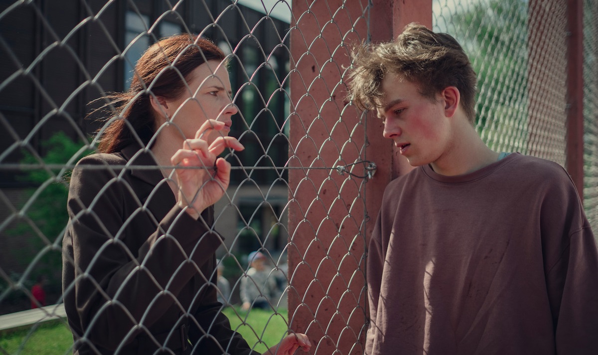 Two teens talk through a chain link fence