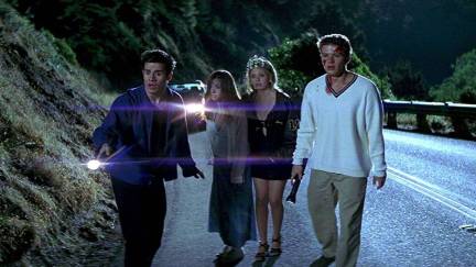 Four teens on a highway look offscreen in horror in 