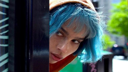 A blue haired woman peers out from a corner in 