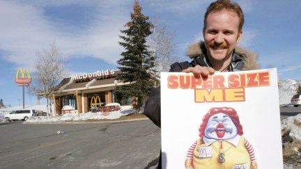 Morgan Spurlock posing outside of a McDonald's with a Super Size Me poster