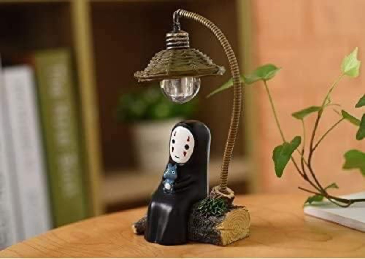 A lamp featuring an adorable No Face from "Spirited Away" sitting on a log 