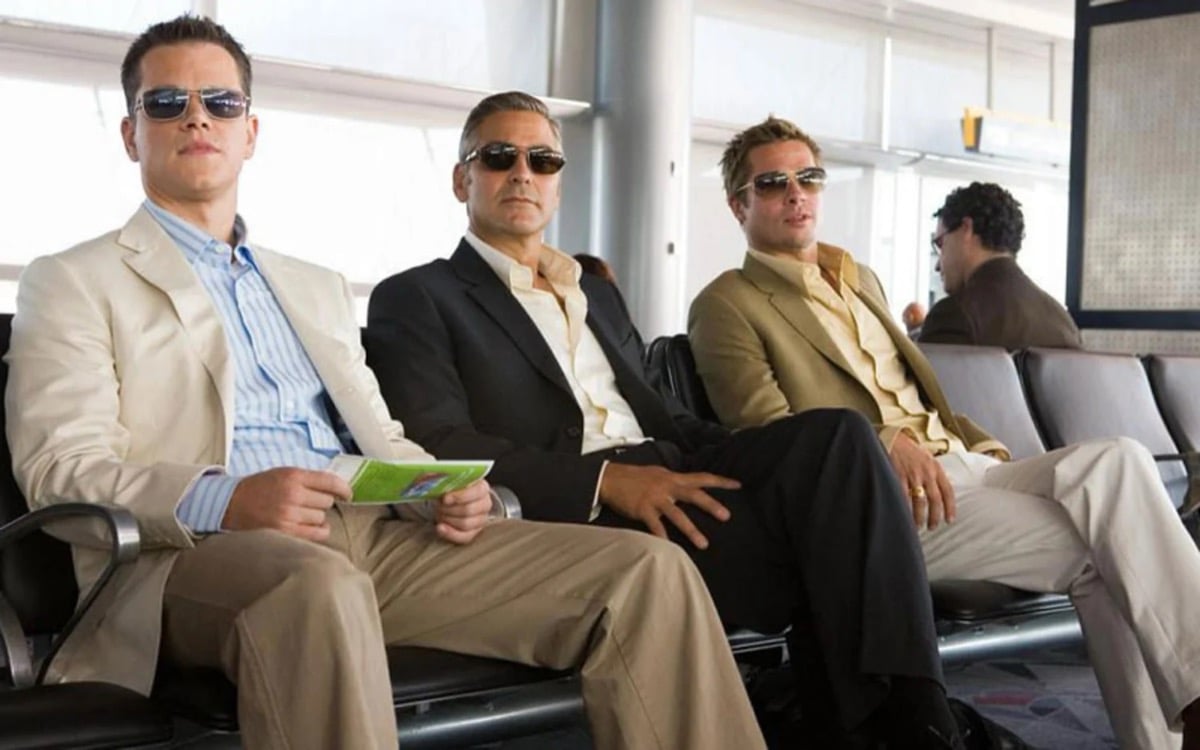 Three well dressed men in sunglasses sit on an airport bench in "Ocean's 13"