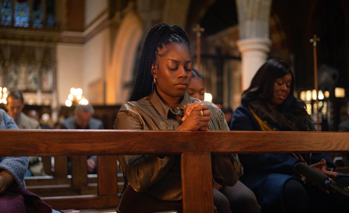 Dionne Brown as Queenie kneels to pray in church