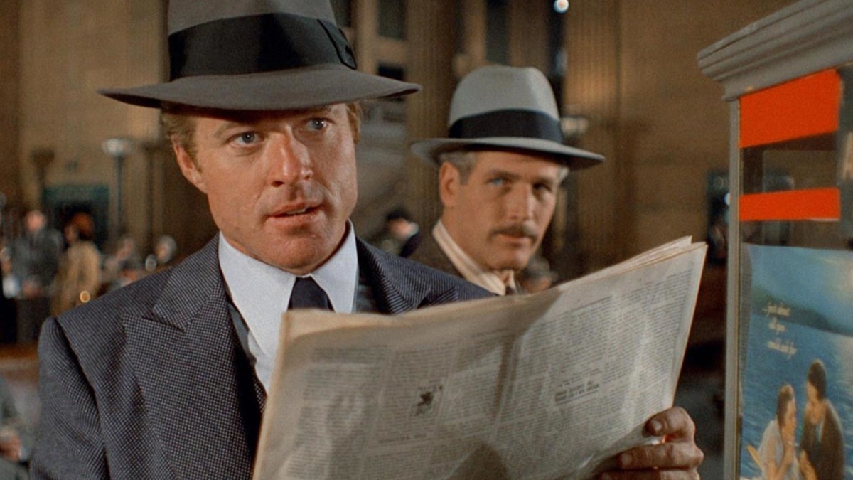 Robert Redford holds up a newspaper while Paul Newman looks on behind him