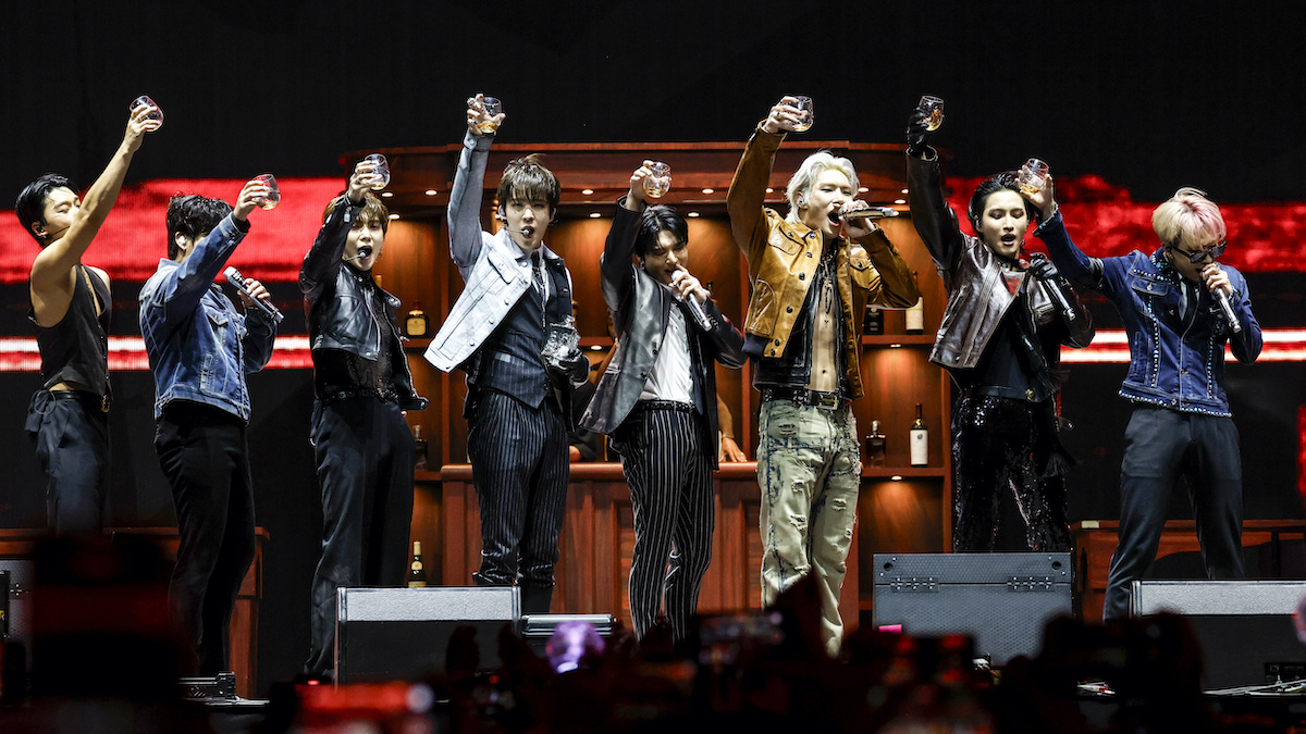 The band ATEEZ performs onstage, each holding up a class toward the audience in a toast