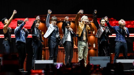 The band ATEEZ performs onstage, each holding up a class toward the audience in a toast