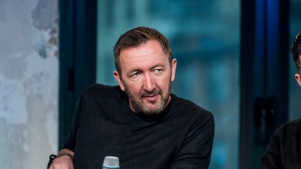 Ralph Ineson holds a microphone on a stage.