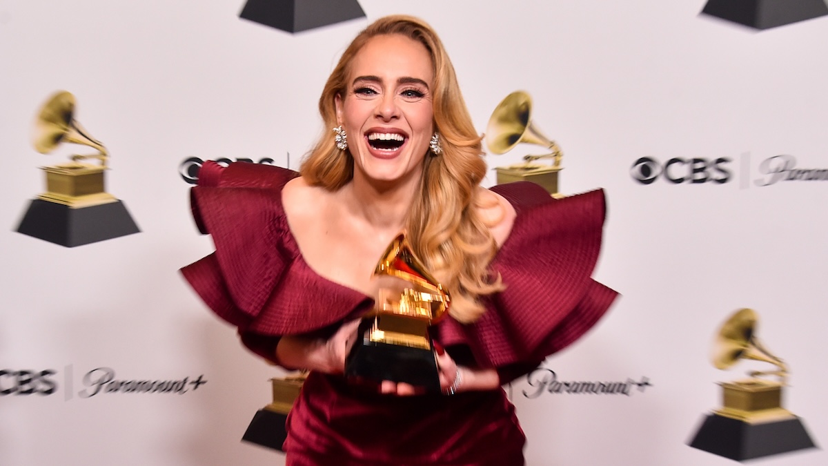 Adele smiling and holding her grammy on a red carpet