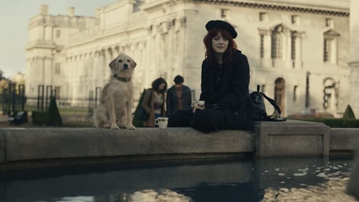 Bobby the dog sitting with Emma Stone in a scene from Cruella