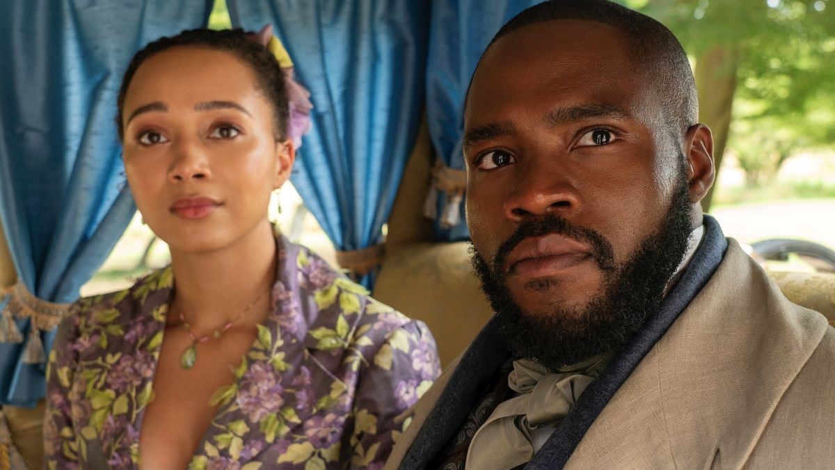 Emma Naomi and Martins Imhangbe as Alice and Will Mondrich in a scene from Netflix's 'Bridgerton.' They are both Black. Alice has her dark hair pulled back into a bun with a pastel floral bow. She's wearing a purple and green floral embroidered jacket with a jade necklace. Will has close-cropped hair and a dark beard and is wearing a beige coat over a black coat and a beige ascot around his neck. They are sitting in a carriage and looking out the window.