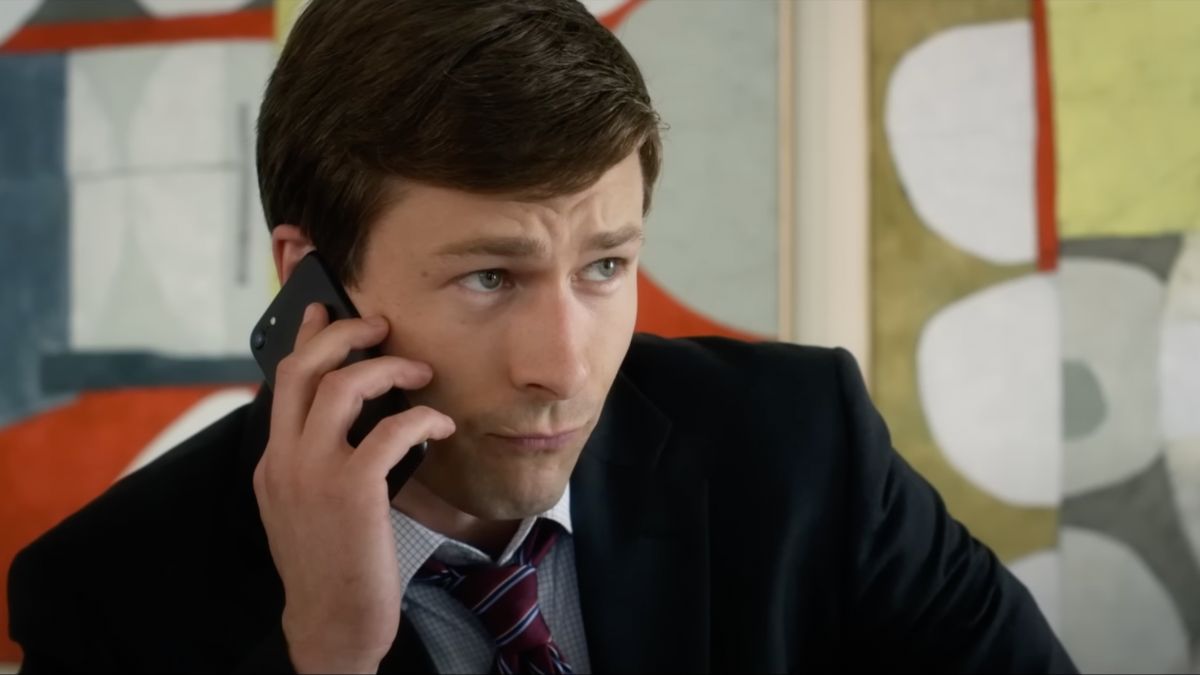 Glen Powell as Charlie in Set It Up is wearing a suit and is on the phone