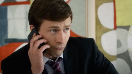 Glen Powell as Charlie in Set It Up is wearing a suit and is on the phone