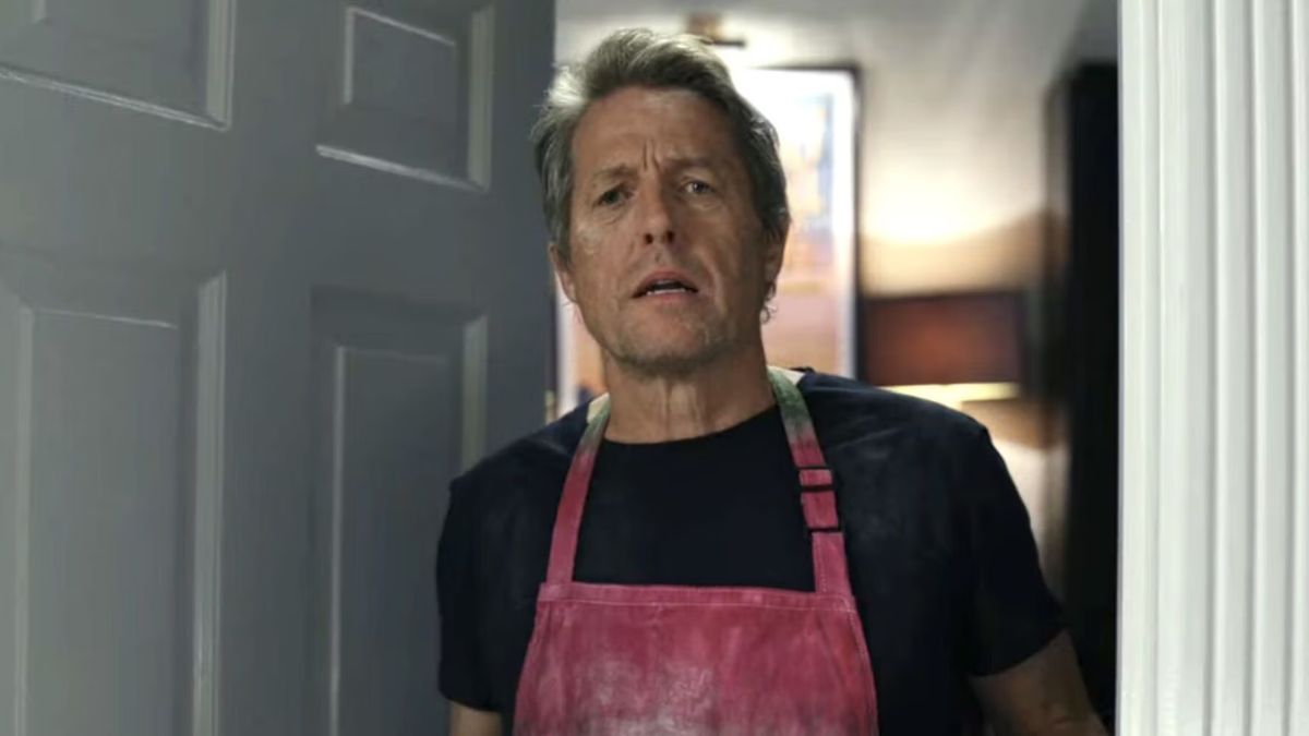 Hugh Grant as Phillip is in an apron, opening the door in Glass Onion: A Knives Out Mystery