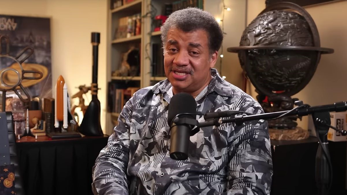 Screencap of Neil deGrasse Tyson in his YouTube show, "Star Talk." He is a Black man with a salt-and-pepper afro and a salt-and-pepper mustache wearing a black-and-white patterned buttondown shirt.