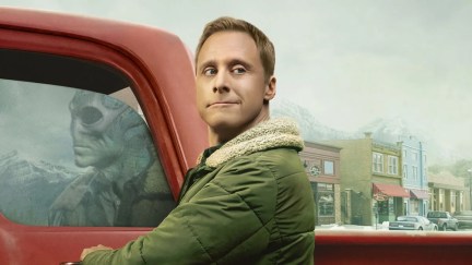 An alien disguised as a human looks over his shoulder while opening his truck door. The reflection in the glass shows his true alien form.