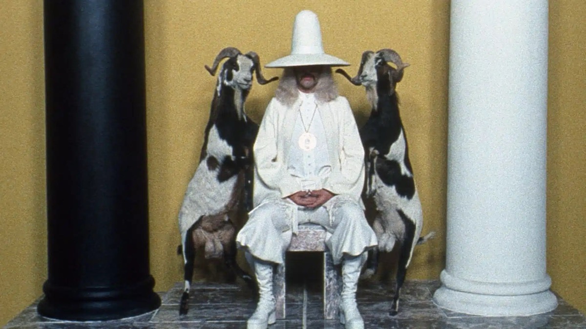 A man in white sits flanked by two ghosts in "The Holy Mountain" 