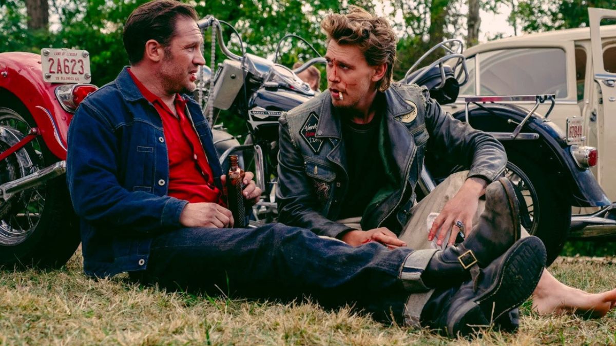 Tom Hardy as Johnny and Austin Butler as Benny sitting on the grass against their bikes in The Bikeriders