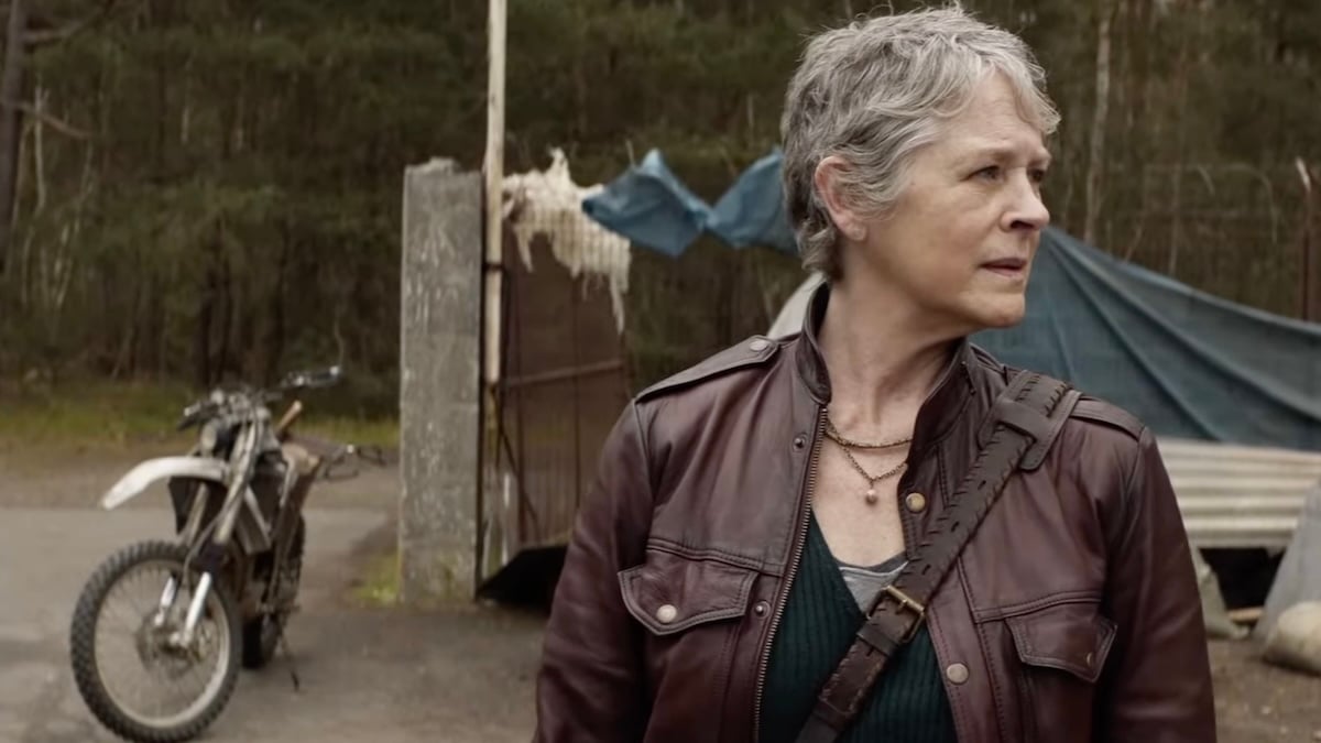 Carol looking over her shoulder standing in front of Daryl's bike