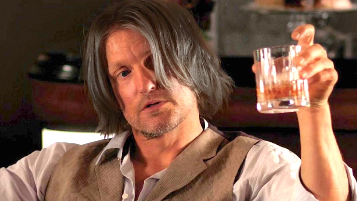 Woody Harrelson as Haymitch in the Hunger Games, raising a glass of what appears to be whiskey.