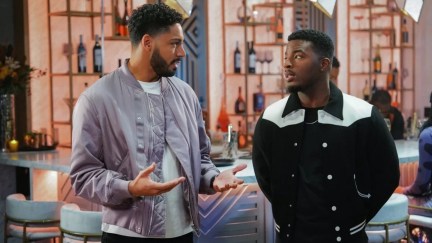 Two men talk to one another in a living room in 