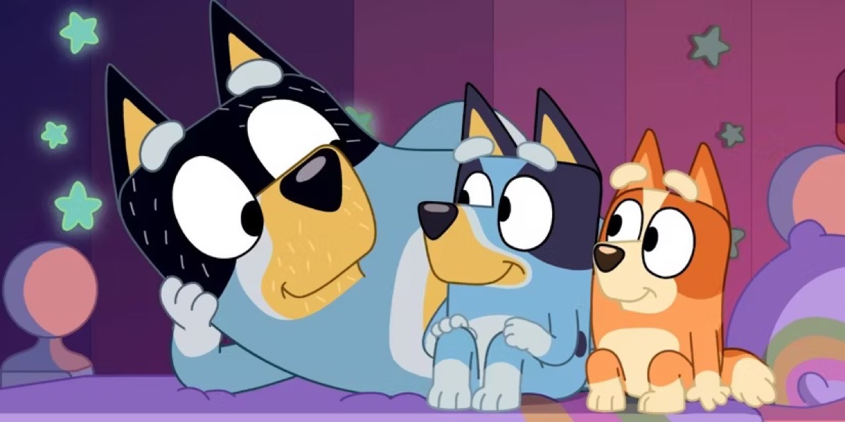 A dog dad smiles laying next to his two dog children in "Bluey" 