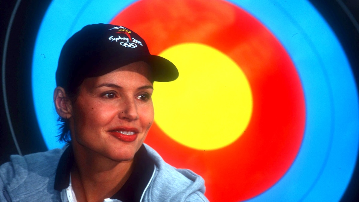 Geena Davis smiles in front of a large archery target.