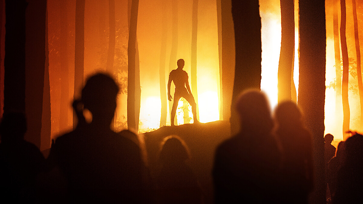 a figure stands silhouetted against a fiery background