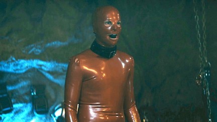 A young man in a latex suit stands in a cave in 