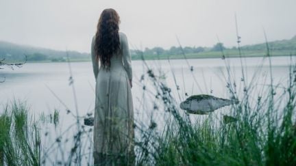 Olivia Cooke as Alicent Hightower clad in a white dress stands in the shallow waters of a lake in House of The Dragon