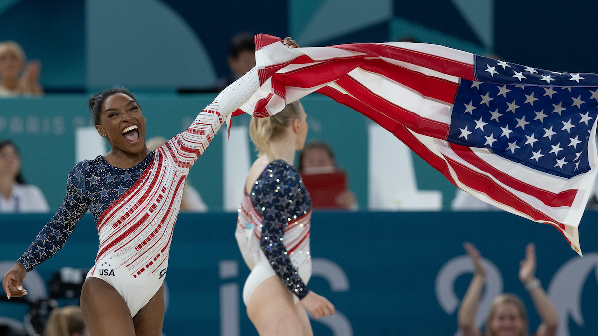 Simone Biles waves an American flag at an Olympic arena