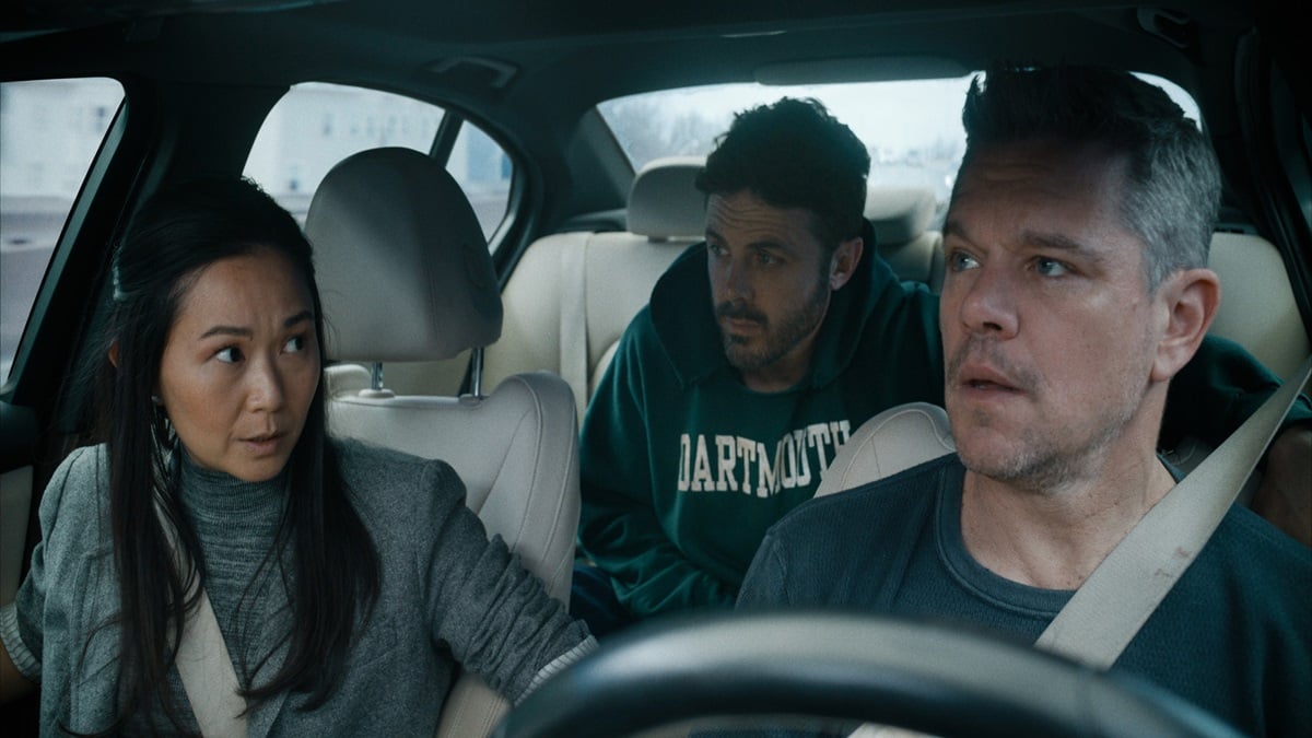 Two men and a woman sit inside a car looking anxious.