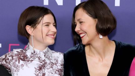 Maggie Gyllenhaal and Jessie Buckley grin at each other on a red carpet.