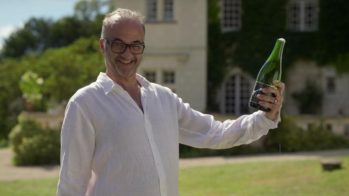 Camille's dad Gerard smiles while holding a champagne bottle