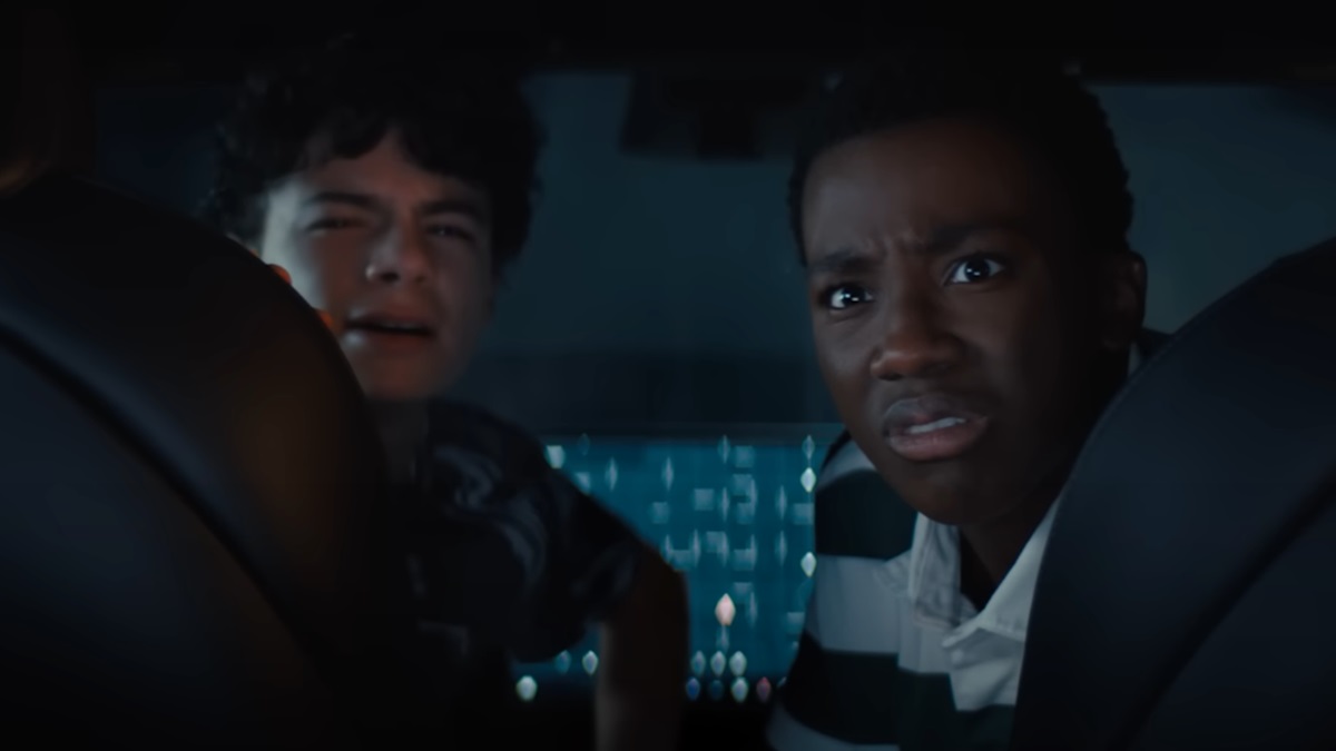 two teen boys look behind them into the backseat with horrified looks on their faces