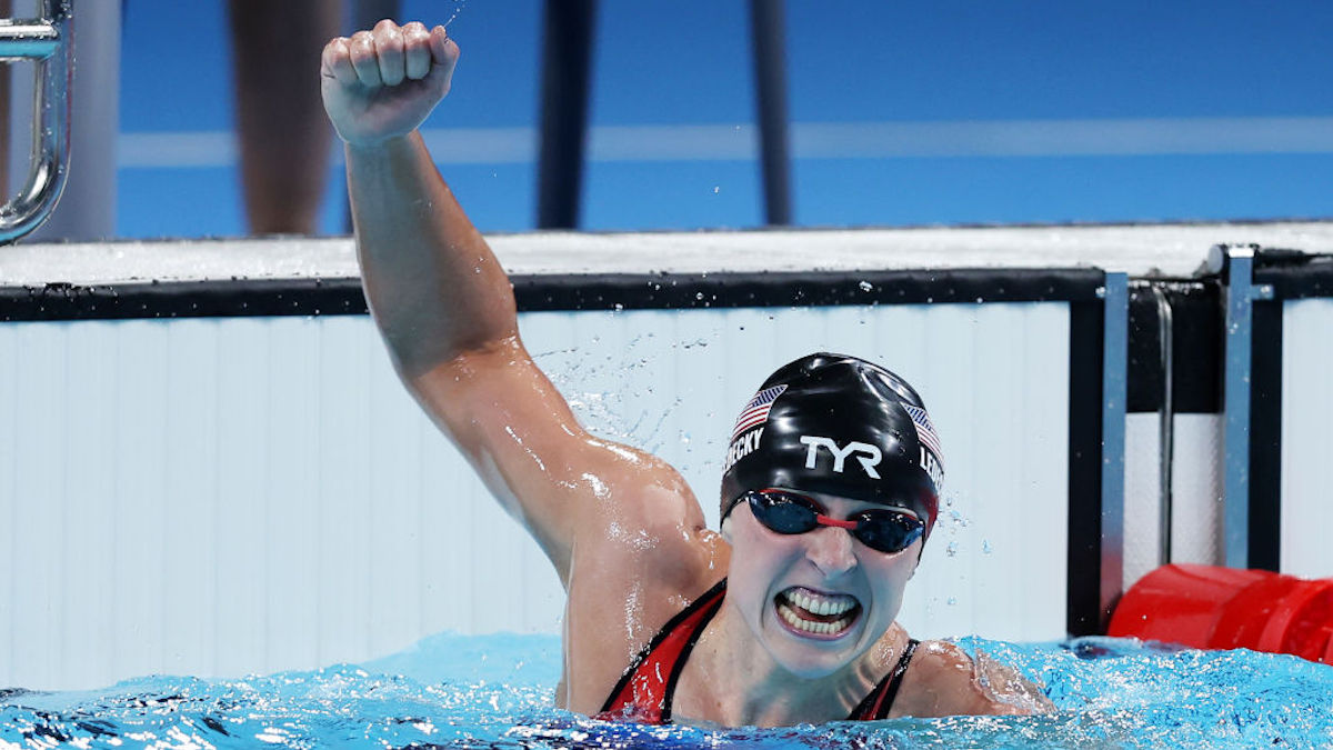 Katie Ledecky raises her hand in triumph in a swimming pool at the Olympics.