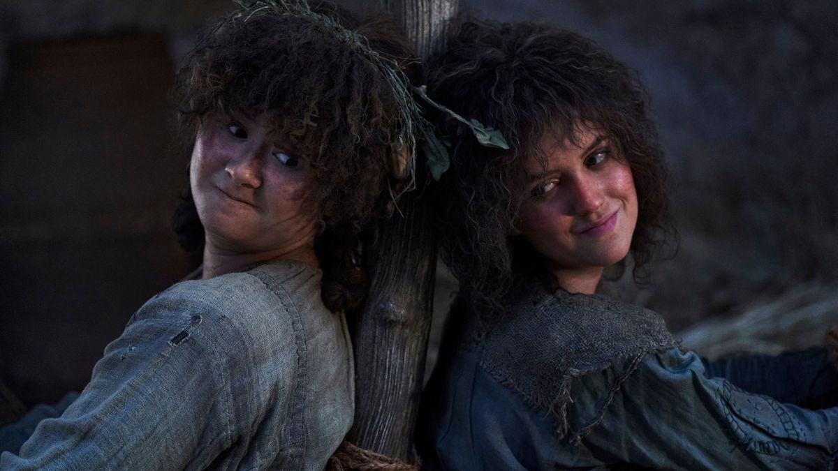 Megan Richards as Poppy Proudfellow and Markella Kavenagh as Nori Brandyfoot sit backs to each other in The Lord of The Rings: The Rings of Power season 2