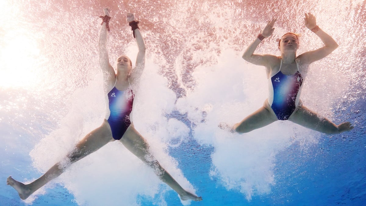 Olympic Divers seen from below as they float in a pool.