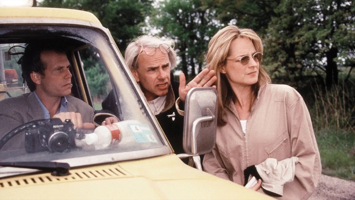 A group of storm chasers talk together surrounding a yellow car in "Twister" 