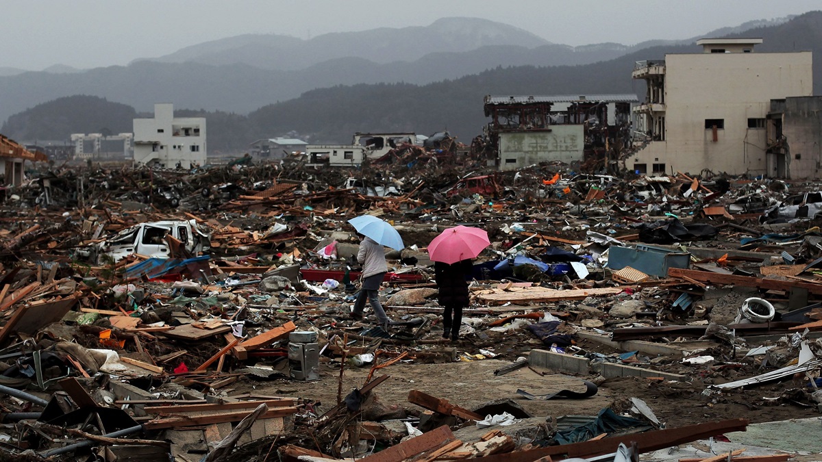 Two people with umbrellas walk through the rubble after a devastating tsunami