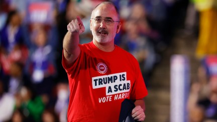 United Auto Workers President Shawn Fain speaks onstage at the DNC wearing a red t-shirt reading 