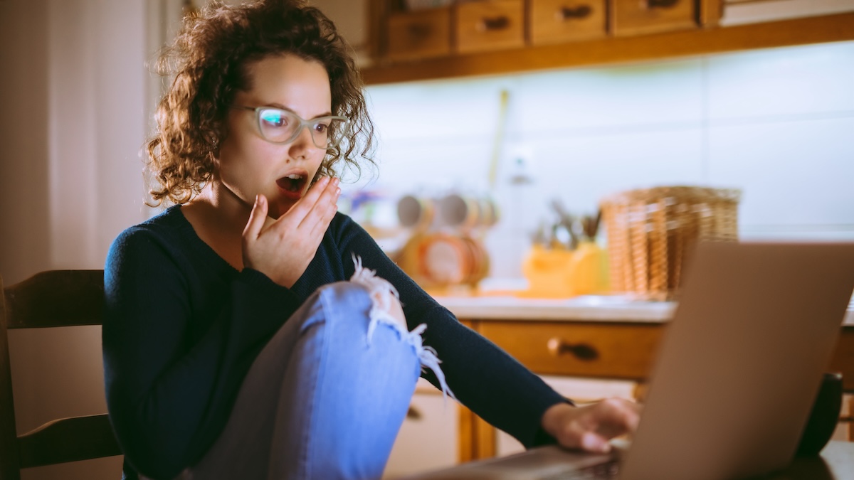 Young brunette woman using laptop at night, looking surprised