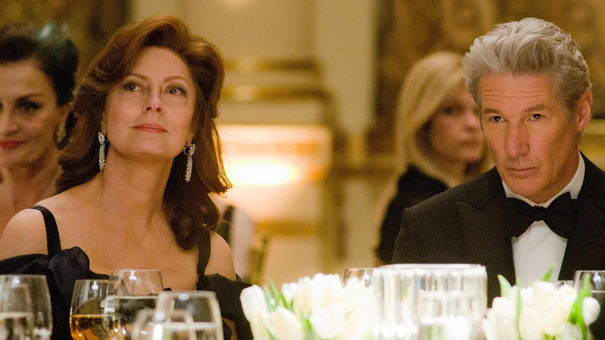 A well to do husband and wife sit at a table at a banquet in "Arbitrage"